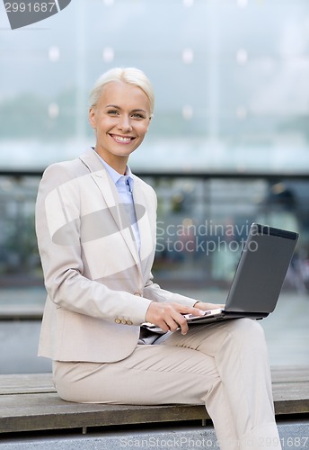 Image of smiling businesswoman working with laptop outdoors