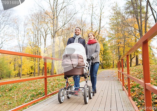 Image of smiling couple with baby pram in autumn park