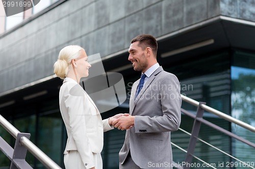 Image of smiling businessmen shaking hands on street