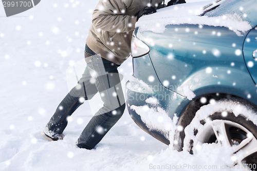 Image of closeup of man pushing car stuck in snow