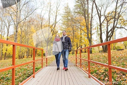Image of smiling couple hugging on bridge in autumn park