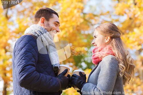 Image of smiling couple with coffee cups in autumn park