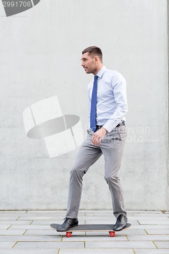 Image of young smiling businessman with skateboard outdoors