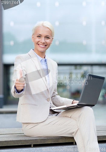 Image of smiling businesswoman working with laptop outdoors