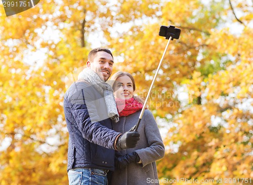 Image of smiling couple with smartphone in autumn park