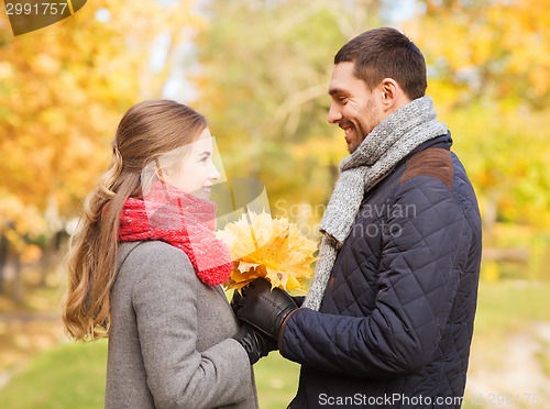 Image of smiling couple with bunch of leaves in autumn park