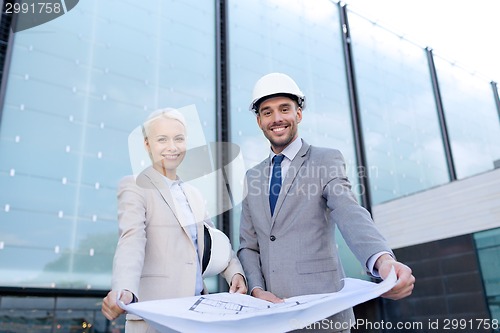 Image of smiling businessmen with blueprint and helmets