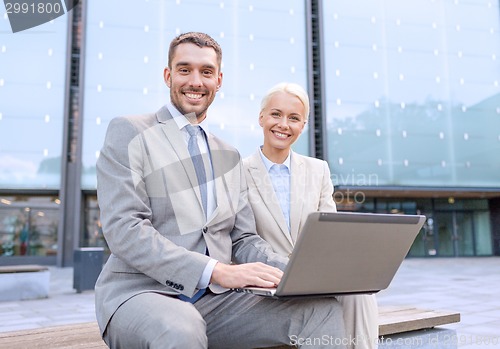 Image of smiling businesspeople with laptop outdoors