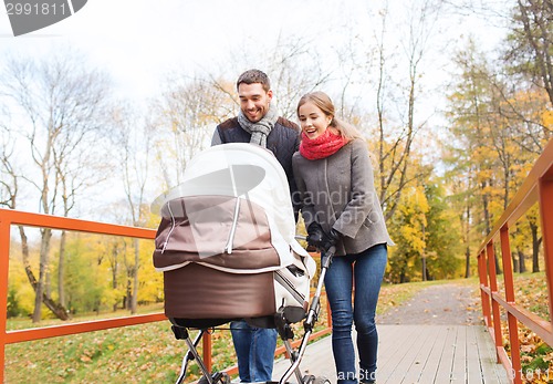 Image of smiling couple with baby pram in autumn park