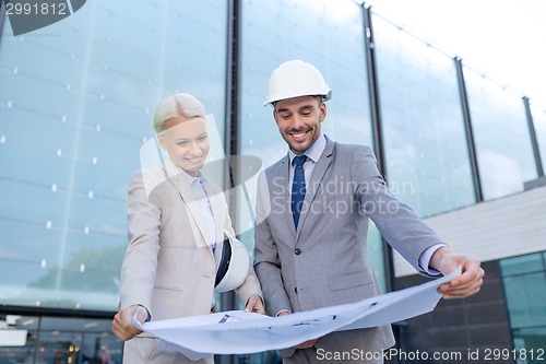 Image of smiling businessmen with blueprint and helmets