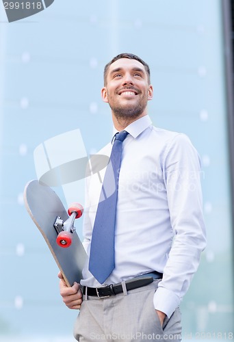 Image of young smiling businessman with skateboard outdoors