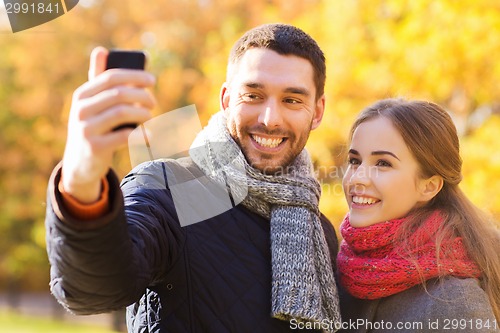 Image of smiling couple with smartphone in autumn park