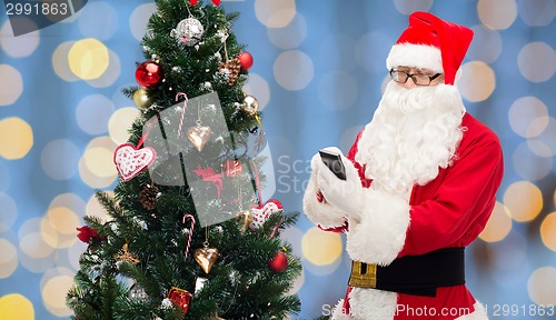 Image of santa claus with smartphone and christmas tree