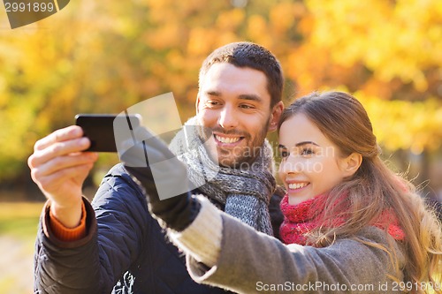 Image of smiling couple with smartphone in autumn park