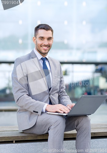 Image of smiling businessman working with laptop outdoors