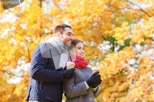 Image of smiling couple with coffee cups in autumn park