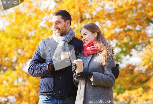 Image of smiling couple with coffee cups in autumn park