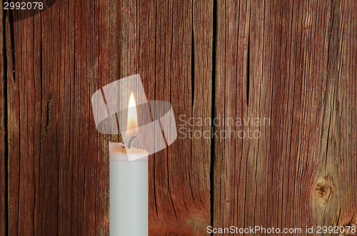 Image of One burning candle at an old red wall
