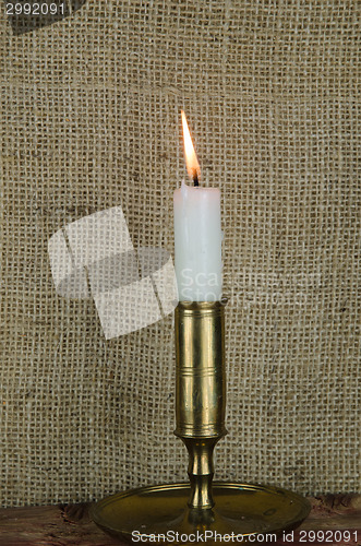 Image of Single candle in candlestick at burlap background