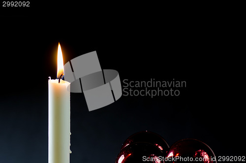 Image of A burning candle with red christmas balls