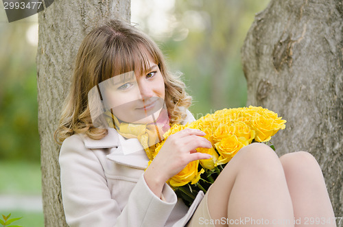 Image of Sad girl with yellow roses, sitting in a tree