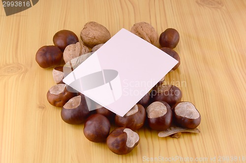 Image of autumn chestnuts on wooden background and blank paper card