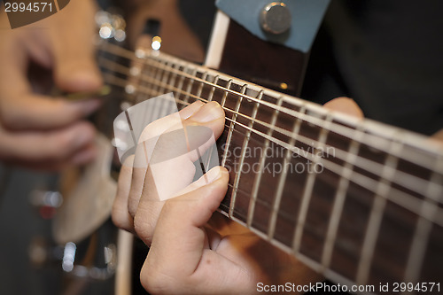Image of close up shot of a man with his fingers on the frets of a guitar