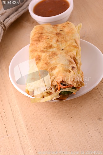 Image of Burrito on white plate with sauce on wooden background
