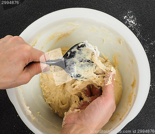 Image of Person handling a sticky dough with black spatula in white plast