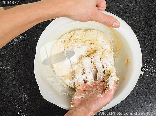 Image of Person kneading a sticky dough in white bowl on black table