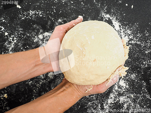 Image of Person holding a proven dough over black table with flour mess