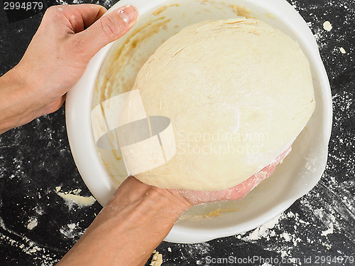 Image of Person lifting a proven dough out from a white plastic bowl on b