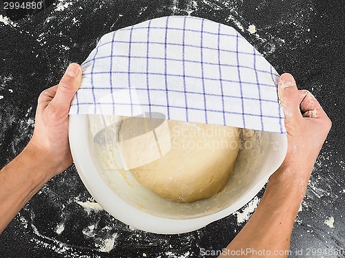 Image of Person covering a dough for proving in a bowl on black table