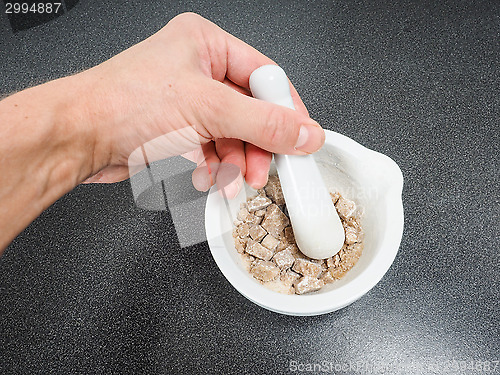 Image of Person crushing brown sugar cubes in a white marble mortar on bl