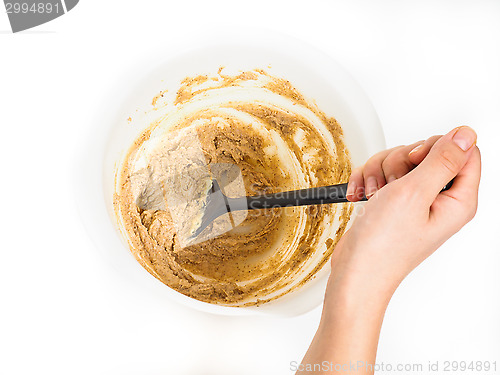 Image of Person stirring a bake mix in white plastic bowl with black spatul