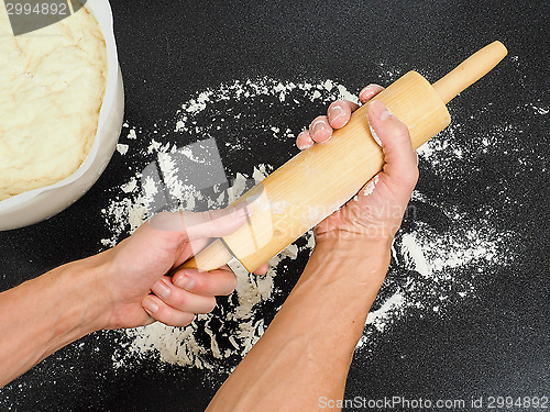 Image of Person preparing a wooden rolling pin with wheat flour before wo