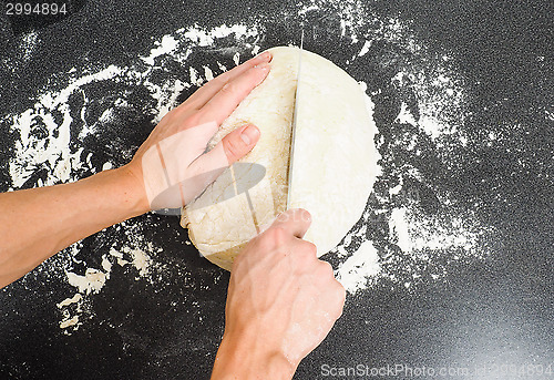 Image of Person cutting a dough into two pieces on a black table with flo