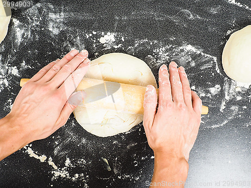 Image of Person handling a dough with a rolling pin floured black table