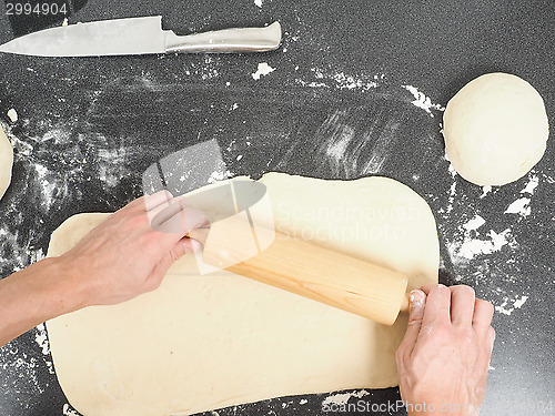 Image of Person handling a dough with a rolling pin floured black table 