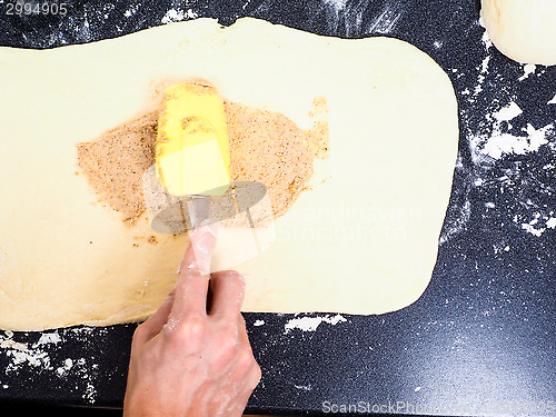Image of Person spreading cinnamon mix with spatula onto a flattened doug