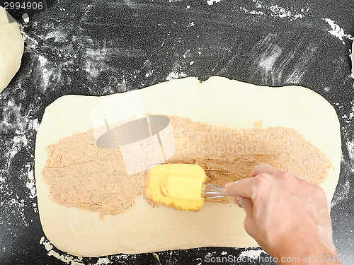 Image of Person spreading cinnamon mix with spatula onto a flattened doug