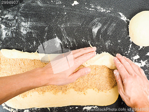 Image of Person rolling a snail bun with sugar and cinnamon spread