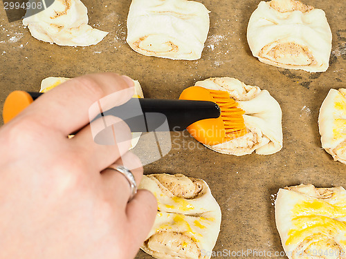 Image of Person glazing plaited baked goods with egg wash
