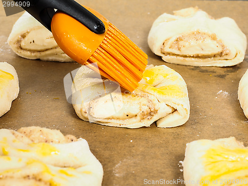 Image of Closeup of person glazing plaited baked goods with egg wash