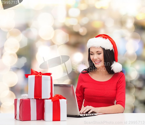 Image of smiling woman in santa hat with gifts and laptop