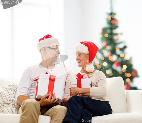 Image of happy senior couple in santa hats with gift boxes