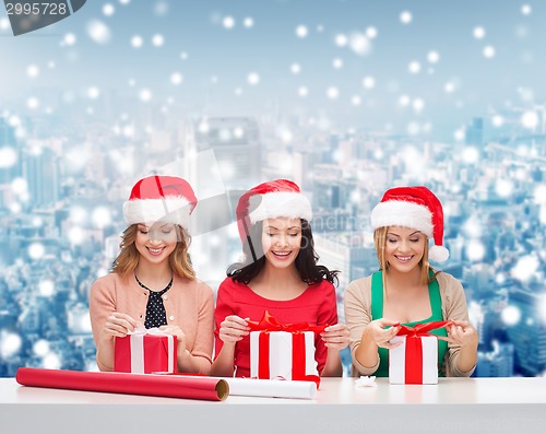 Image of smiling women in santa helper hats packing gifts