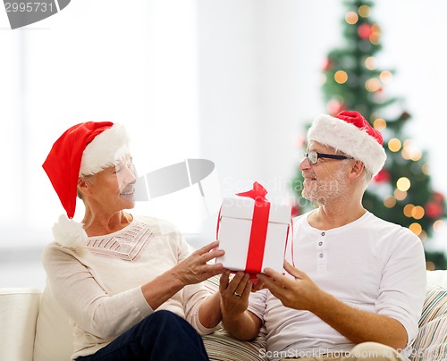 Image of happy senior couple in santa hats with gift box