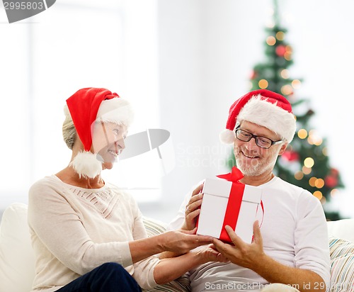 Image of happy senior couple in santa hats with gift box