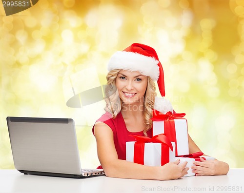 Image of smiling woman in santa hat with gifts and laptop